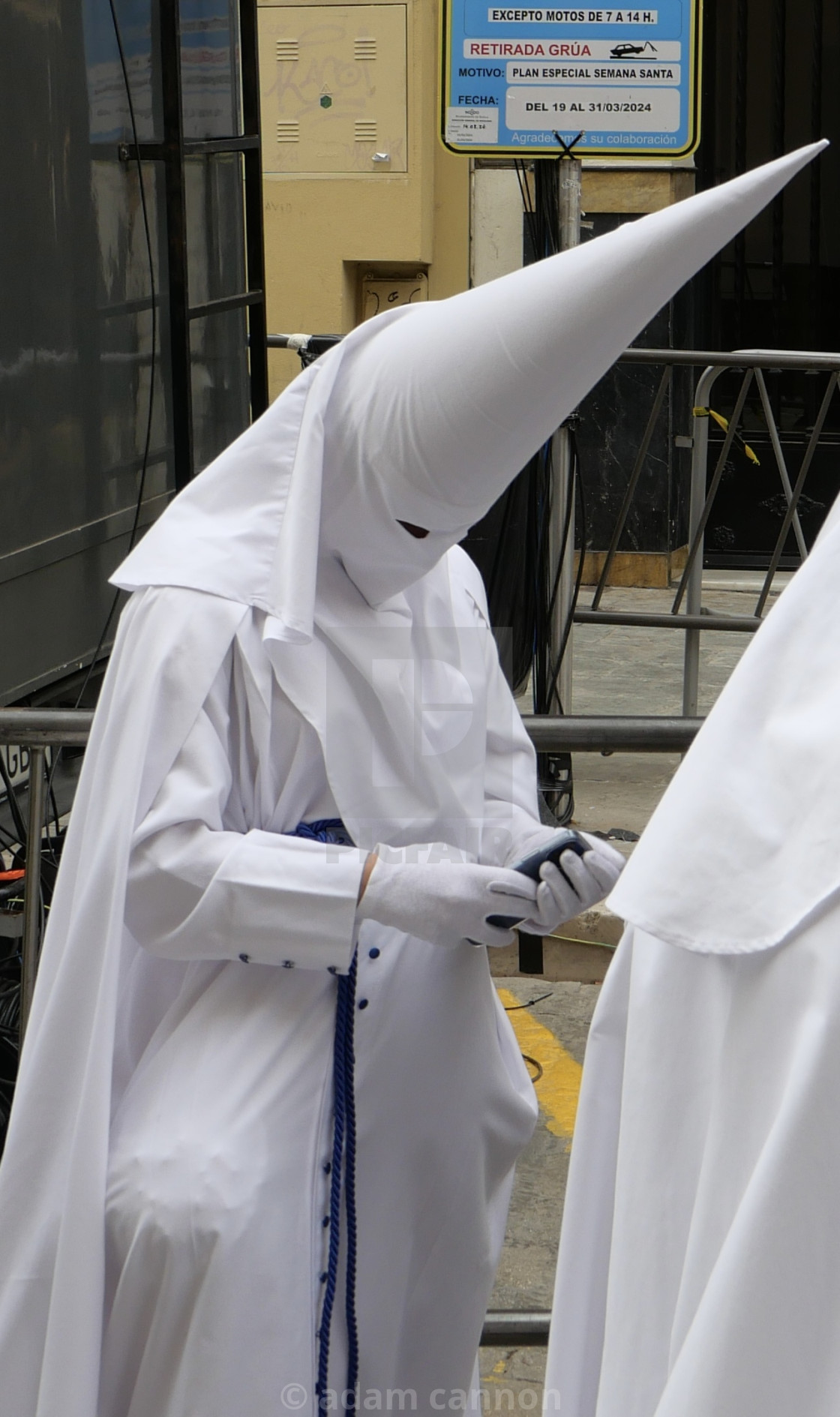 "a boy in a white capirote and on his phone - palm sunday, seville" stock image