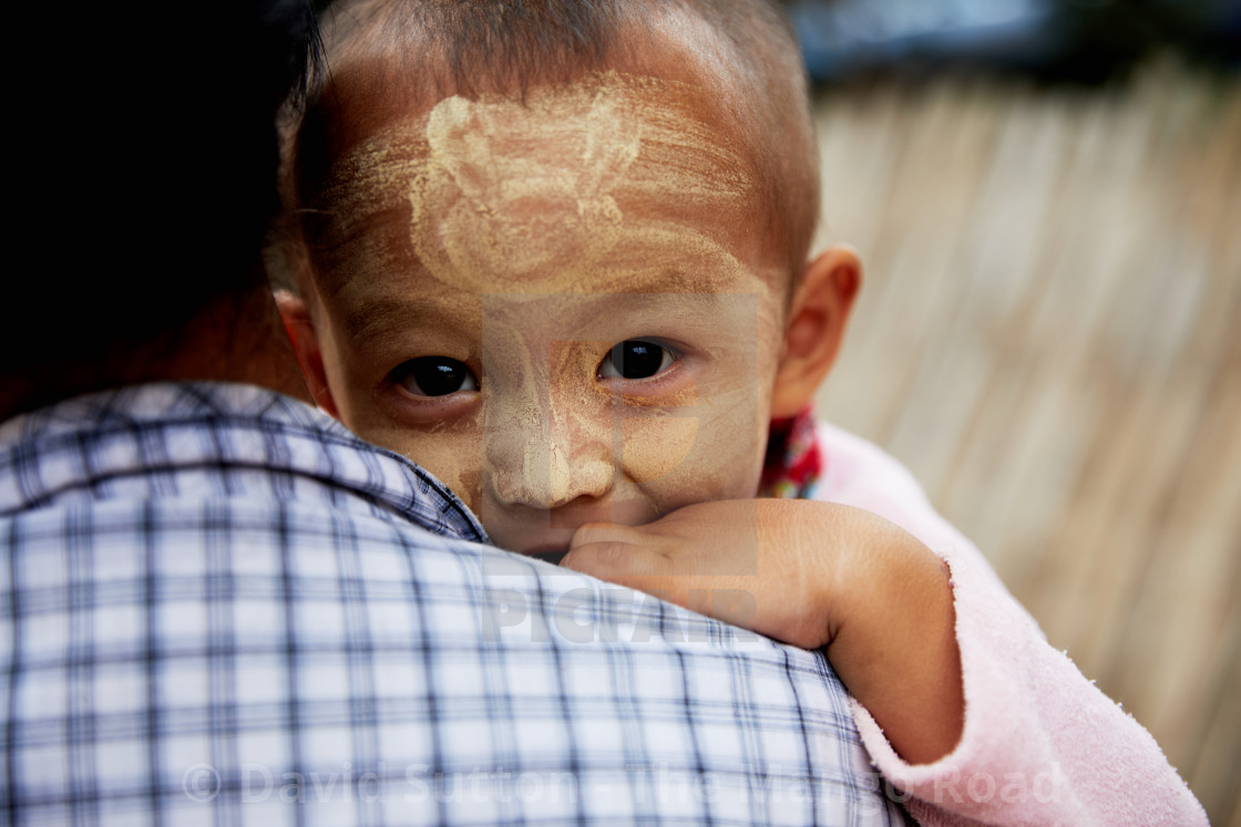 "Young boy peers over his mothers shoulder and the village of Taungbi, near..." stock image