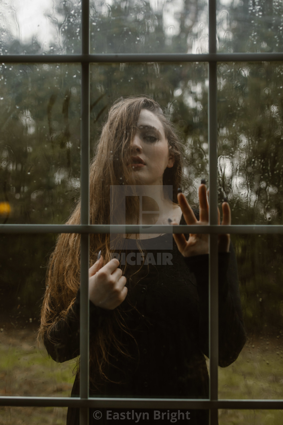 Young Woman Looking Through A Wet Window On A Rainy Day
