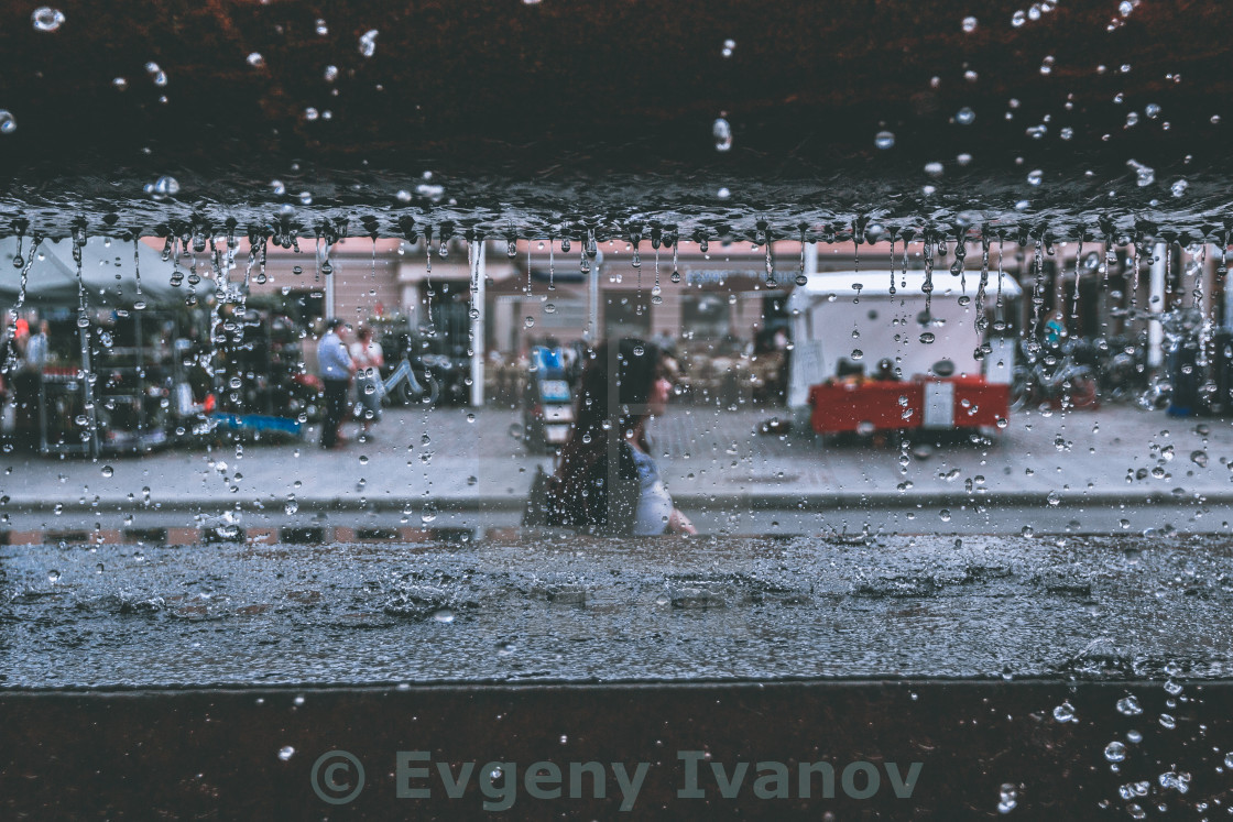 "Girl walking on the street seen through fountain water drops" stock image