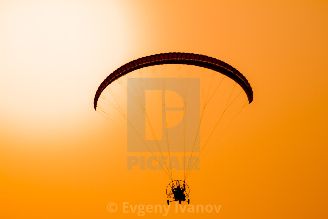 "Paraglider flying with paramotor on dramatic sunset sky with big sun in orange and yellow. Concept for adventure extreme ultra light aviation" stock image