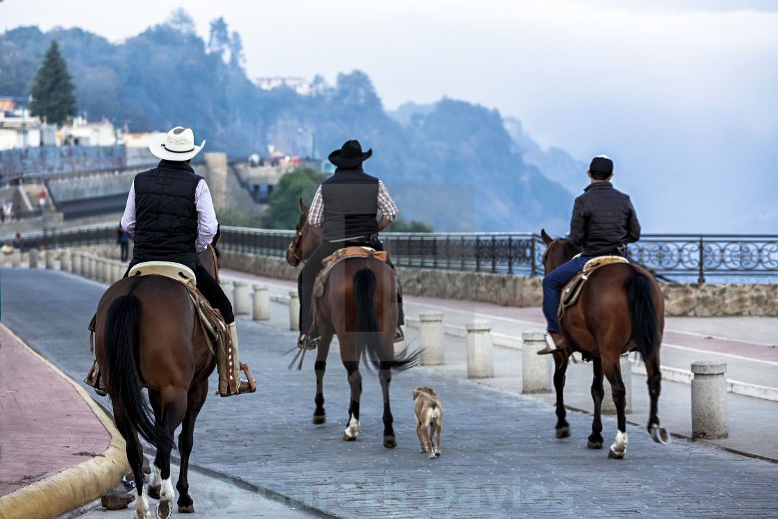 "3 men on horseback riding through a small village" stock image