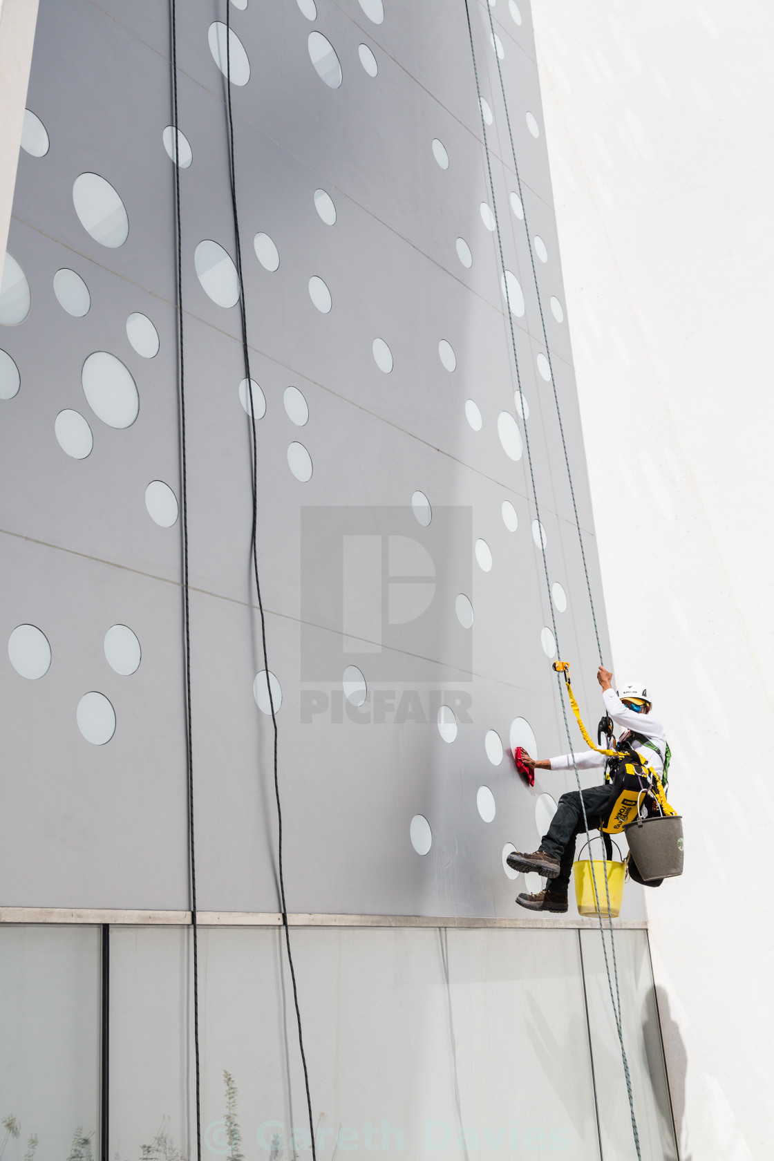 "a man cleans a window of a building suspended by a rope" stock image