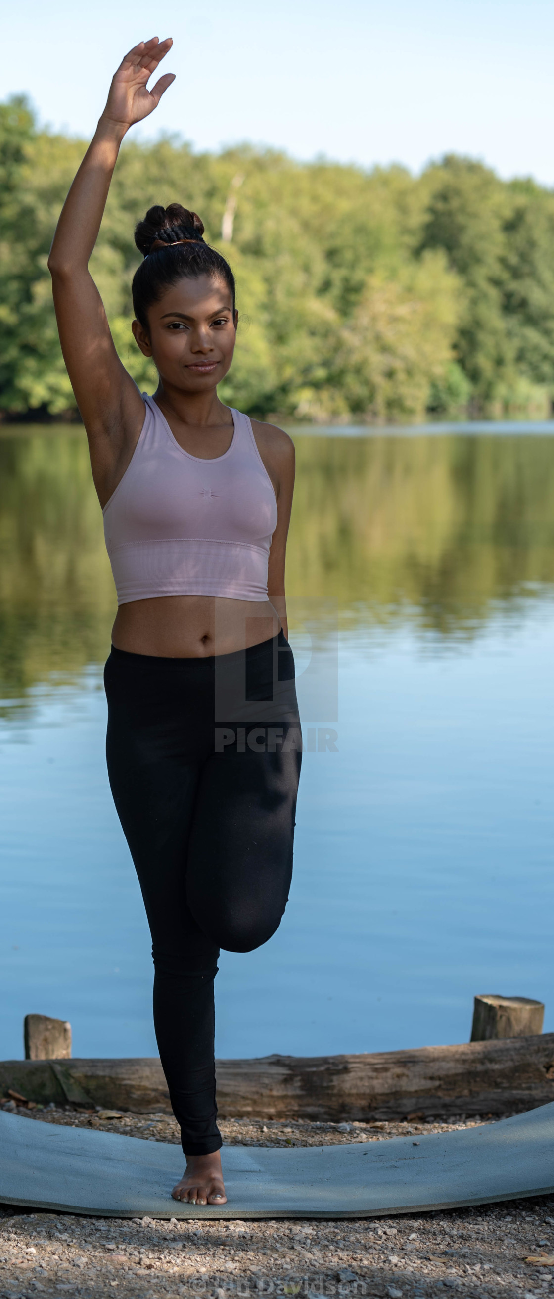 "Young woman performs yoga by lake" stock image