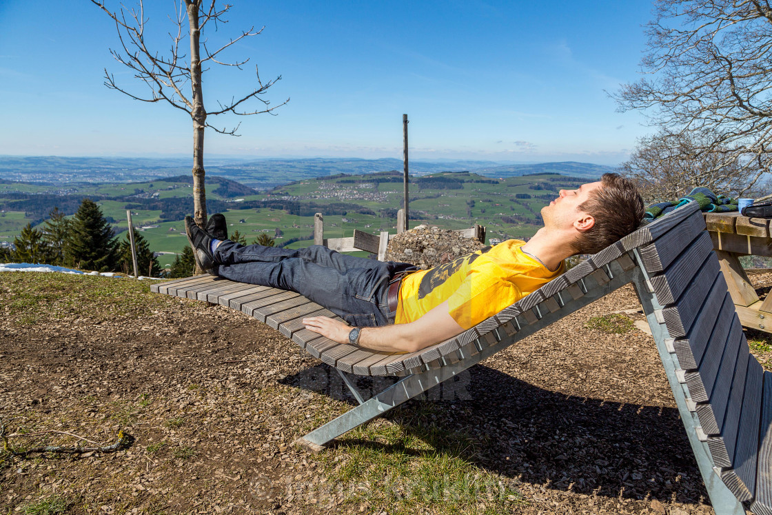 "Young man lying on a wooden chair in the nature on the hill with a great view..." stock image