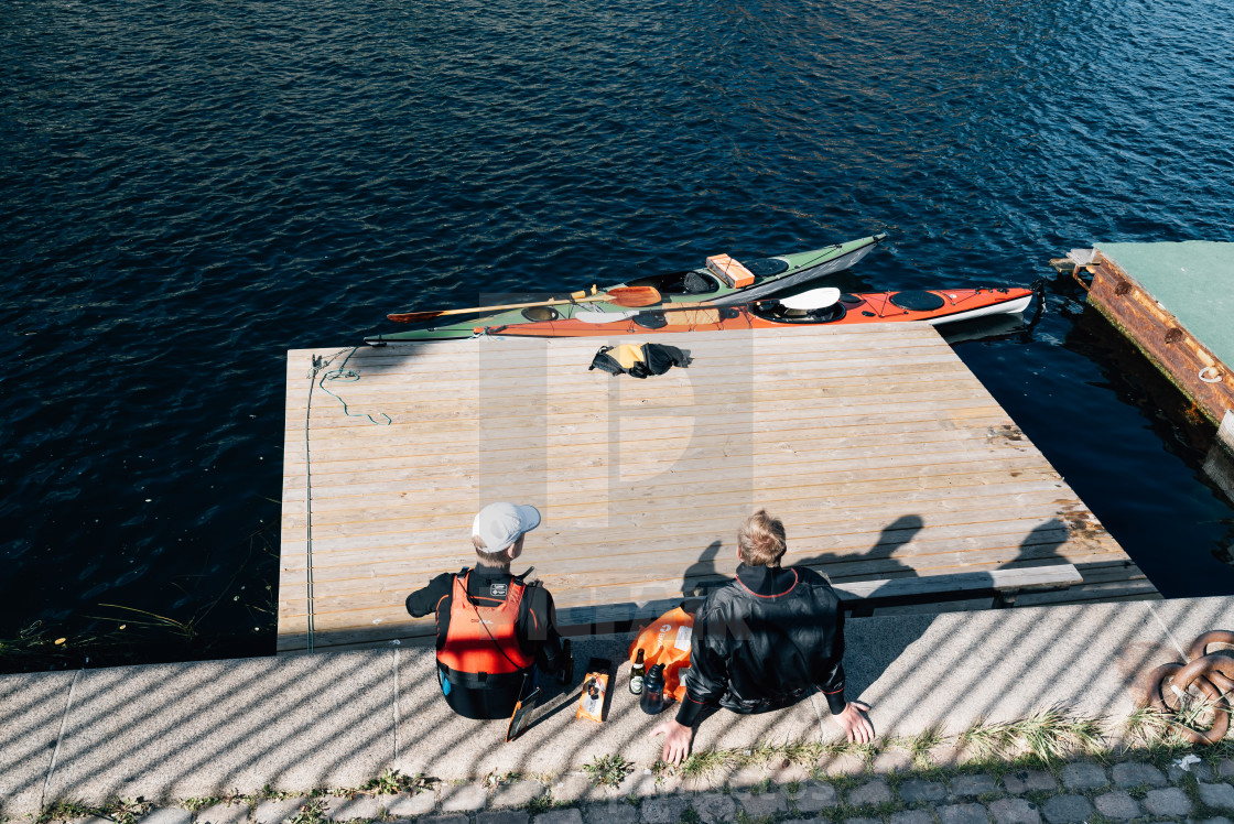 "Canoeists resting after exercise sitting on waterfront" stock image