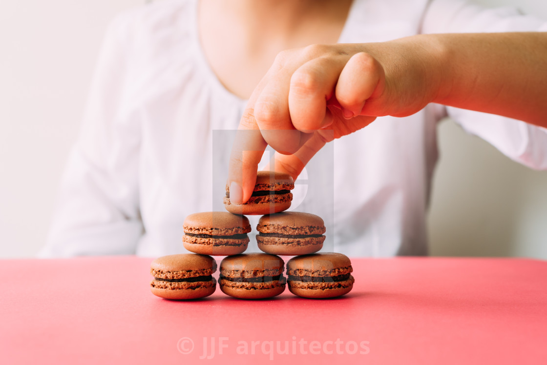 "Woman placing macaroons on heap on pink table" stock image