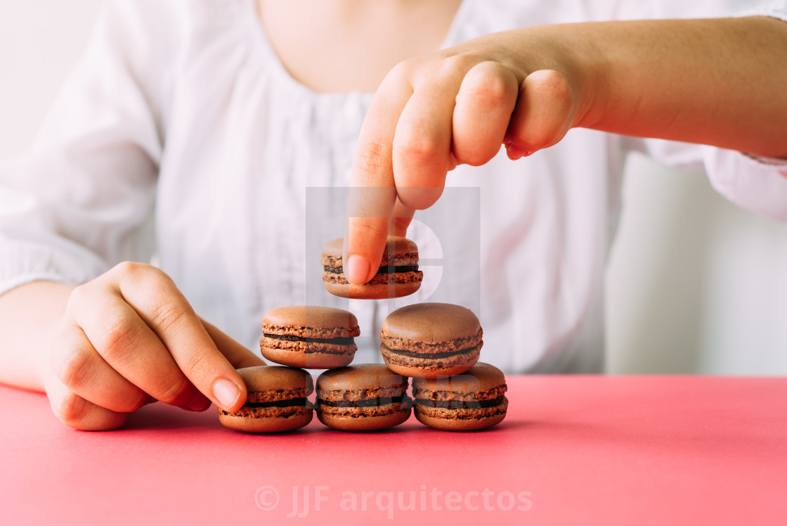 "Woman placing macaroons on heap on pink table" stock image