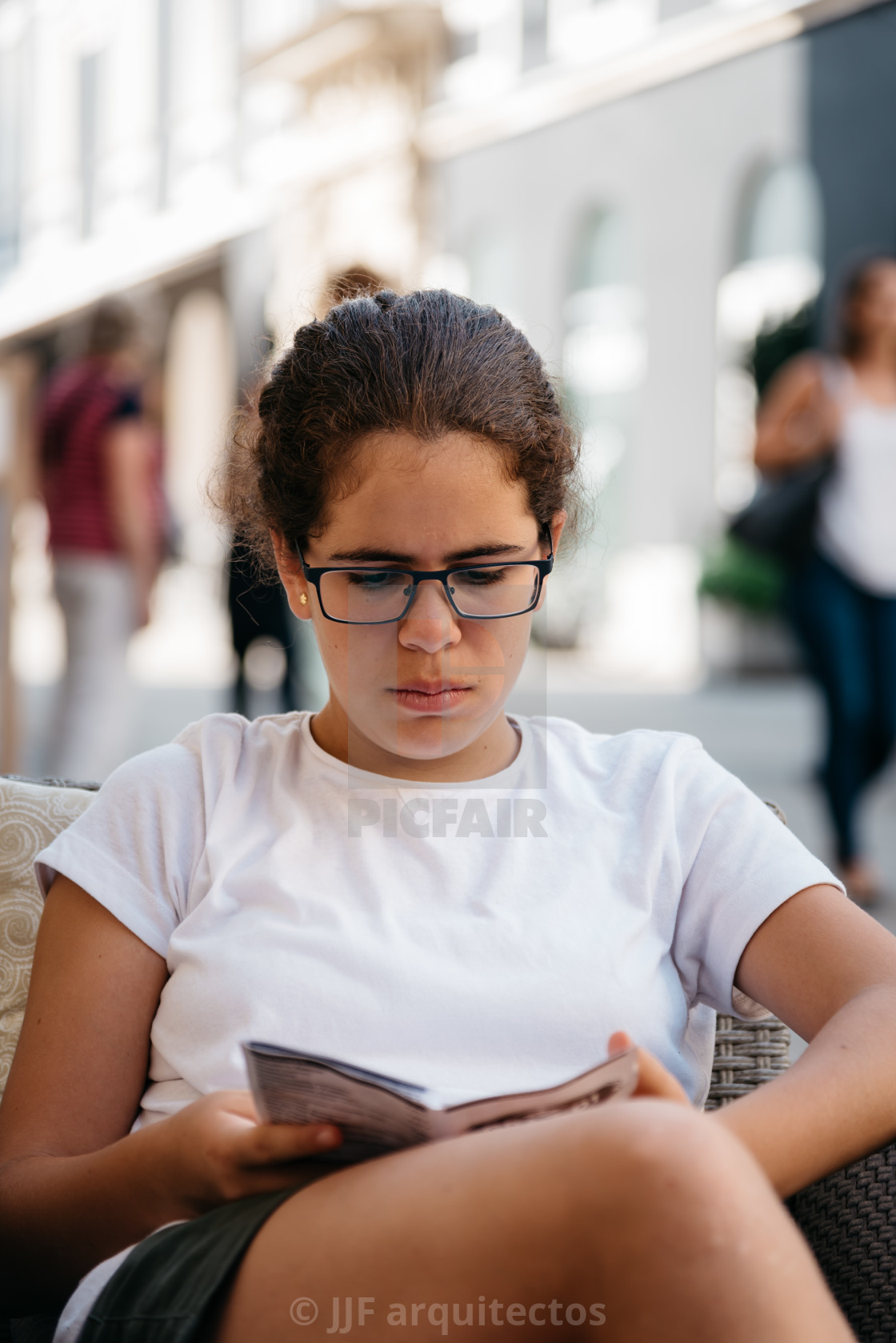 "Girl wearing glasses reading sitting in the street" stock image