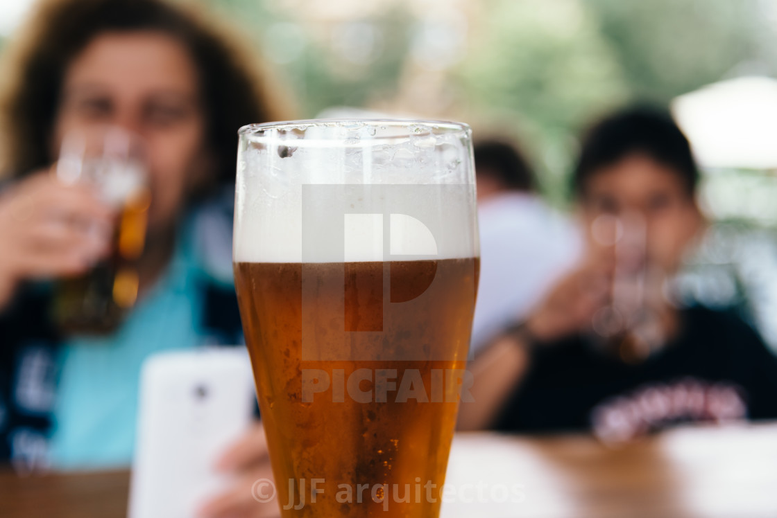 "Close up of refreshing pint of lager beer against family in bar" stock image