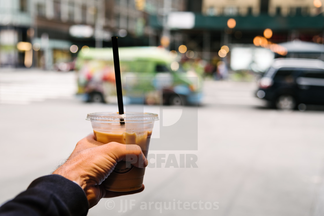 "Male hand holding cup of coffee against cityscape" stock image