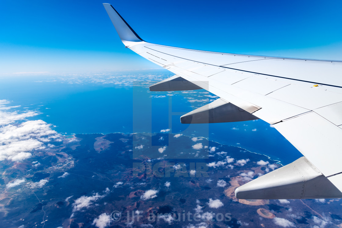 "Wing of airplane above island with blue sky" stock image