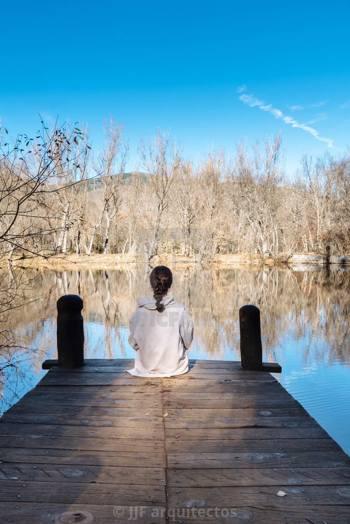 "Young woman sitting on pier by the lake" stock image