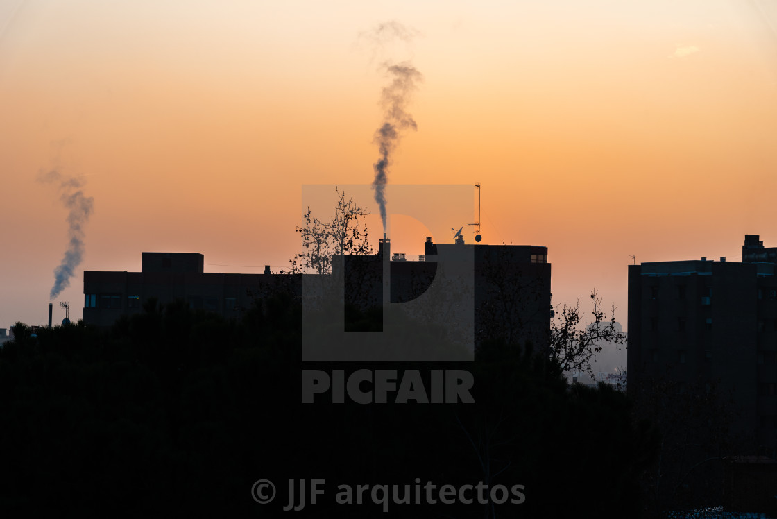 "Urban landscape with the silhouette of buildings with chimneys expelling smoke at sunset" stock image