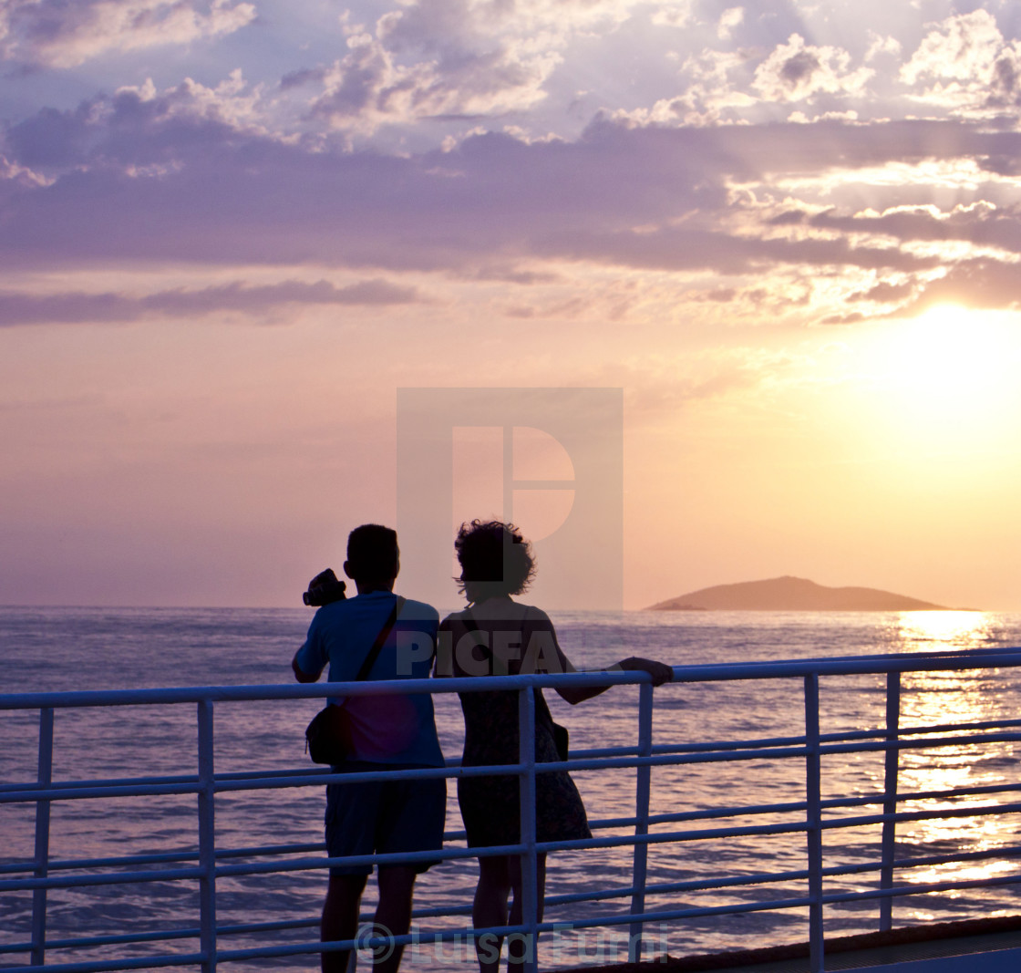 "Couple looking at sunset on sea and shooting pictures from ferry deck" stock image