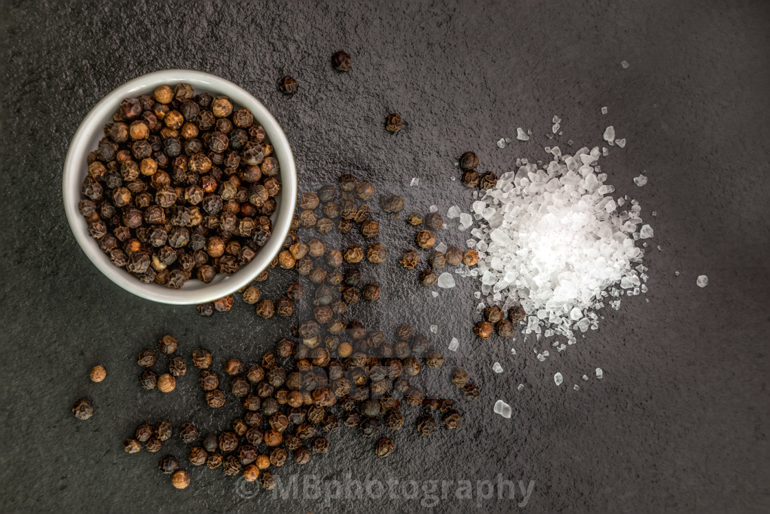 "Sea salt and pepper grains on dark stone surface, close up" stock image