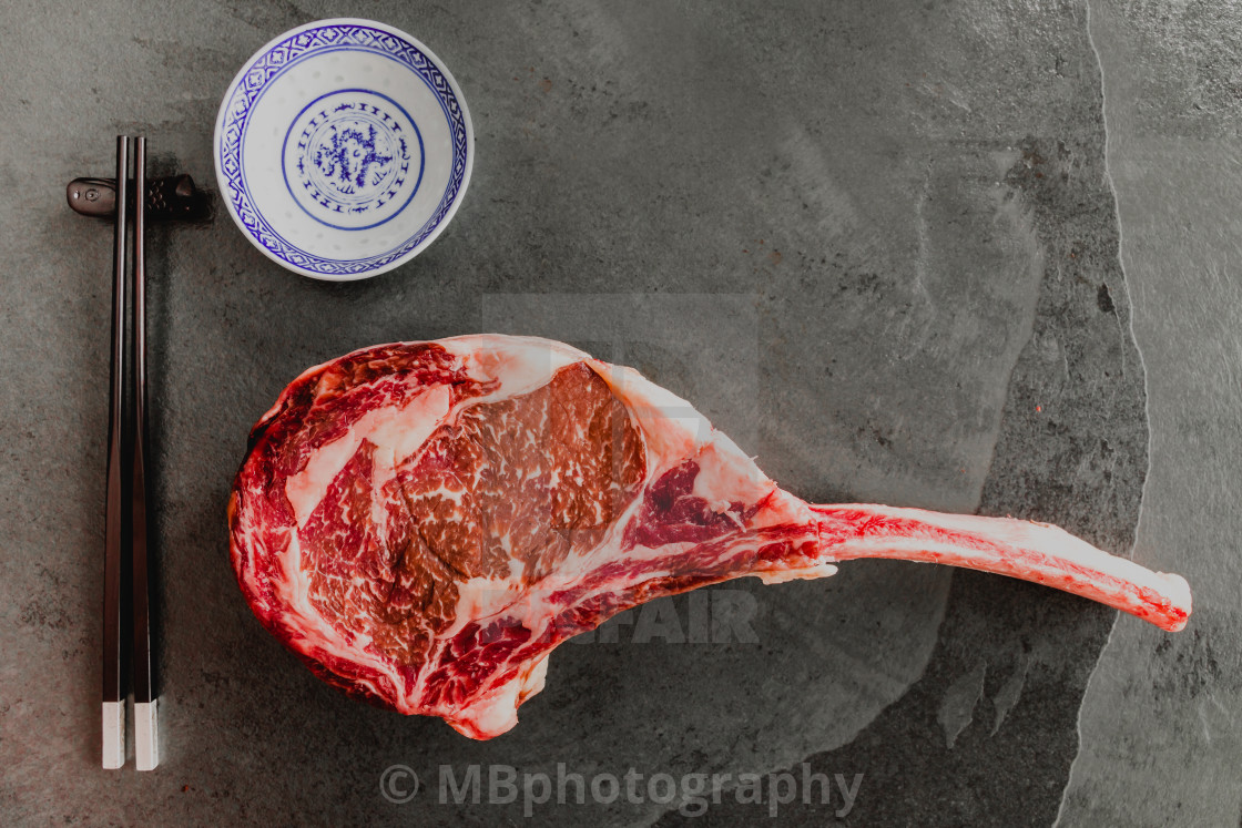 "Big sushi. Raw, dry-aged wagyu tomahawk steak on a black stone" stock image