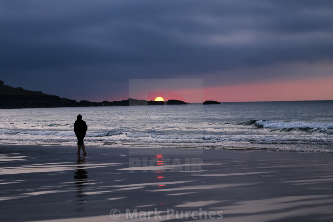 "Silhouette of Man in Hoodie Walking Alone on St Ives Beach During Sunset" stock image