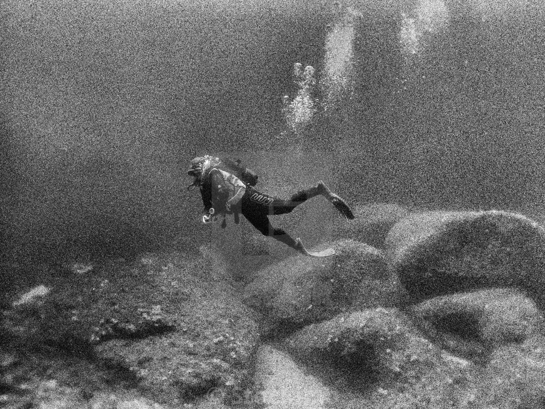 "Young female scuba diver swimming over limestone rocks at depth" stock image