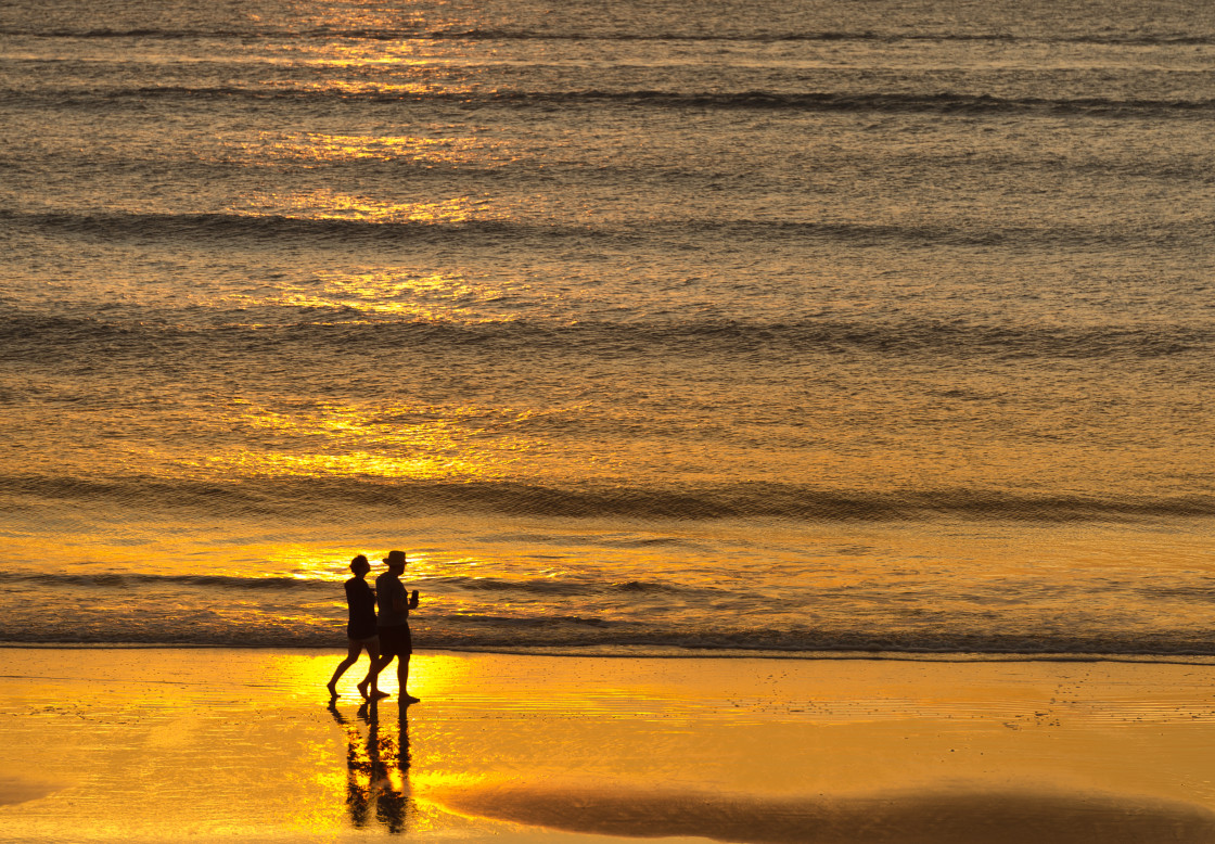 "Couple walking at sunrise on the beach" stock image