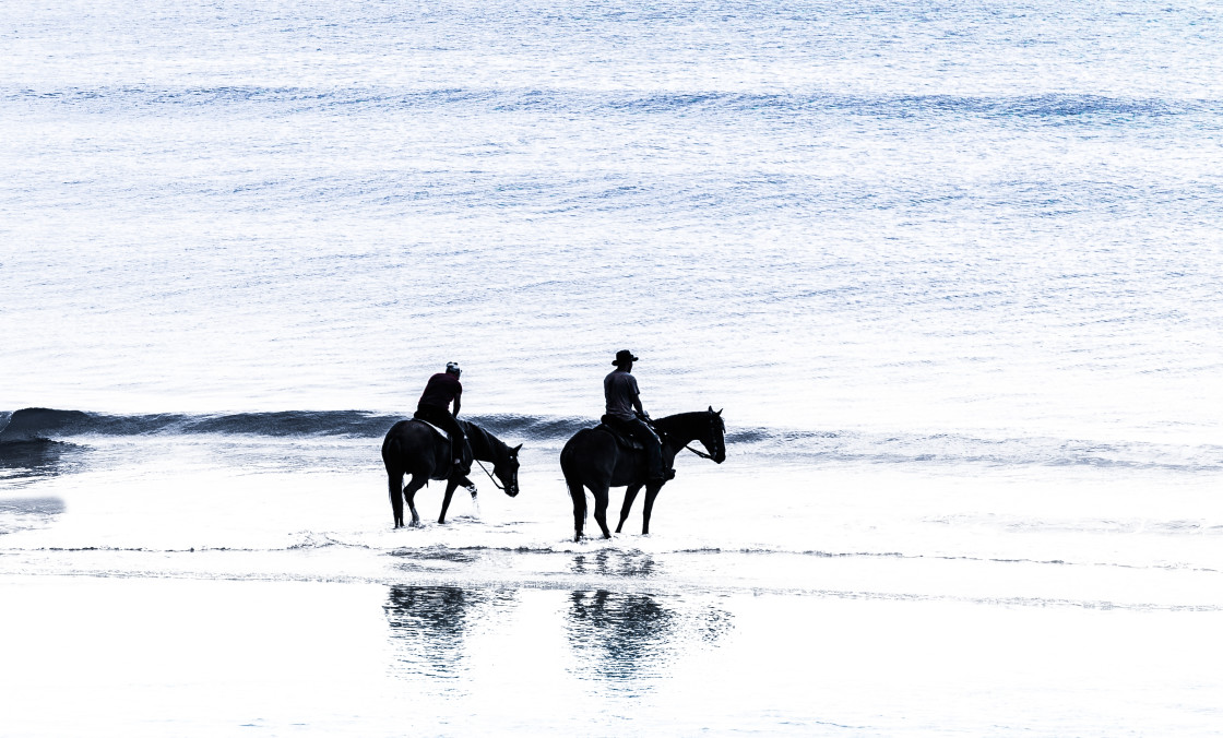 "Men on horses at beach sunrise" stock image