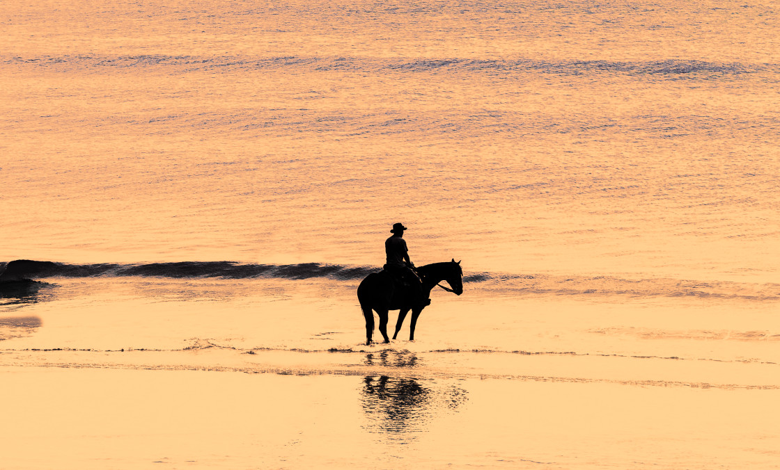 "Man on horseback at beach sunrise" stock image