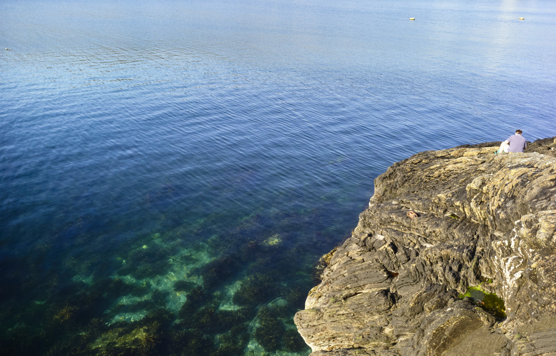 "A lone fisherman sitting on a rock" stock image