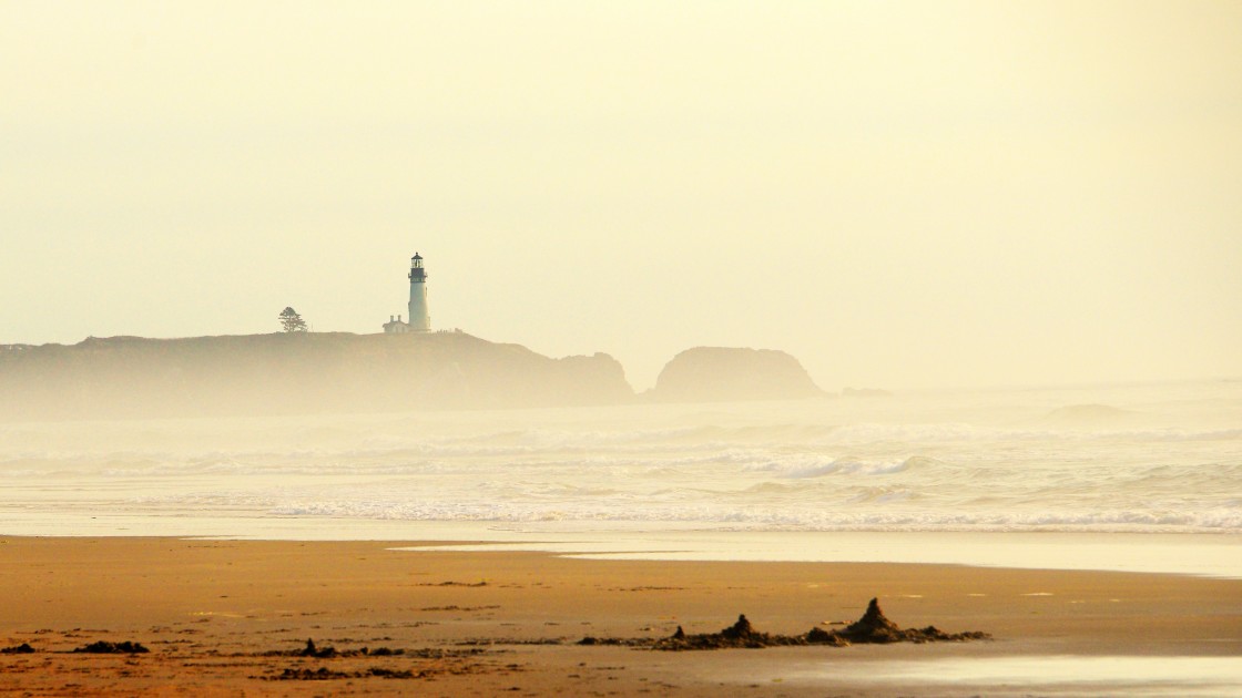 "View of a misty beach with a lighthouse in the distance at the Oregon Coast." stock image