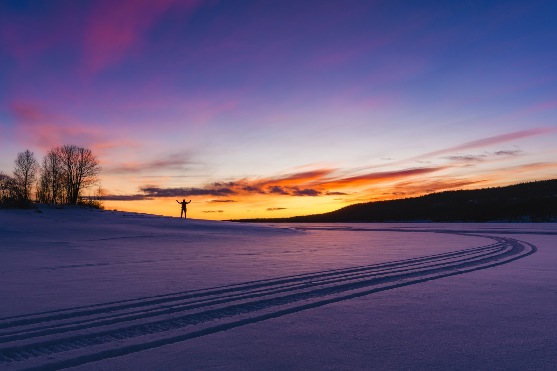 "Man standing on frozen and snow covered lake at sunrise" stock image