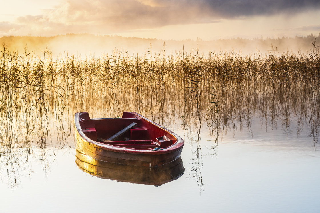 "Red boat on still misty lake at sunrise" stock image