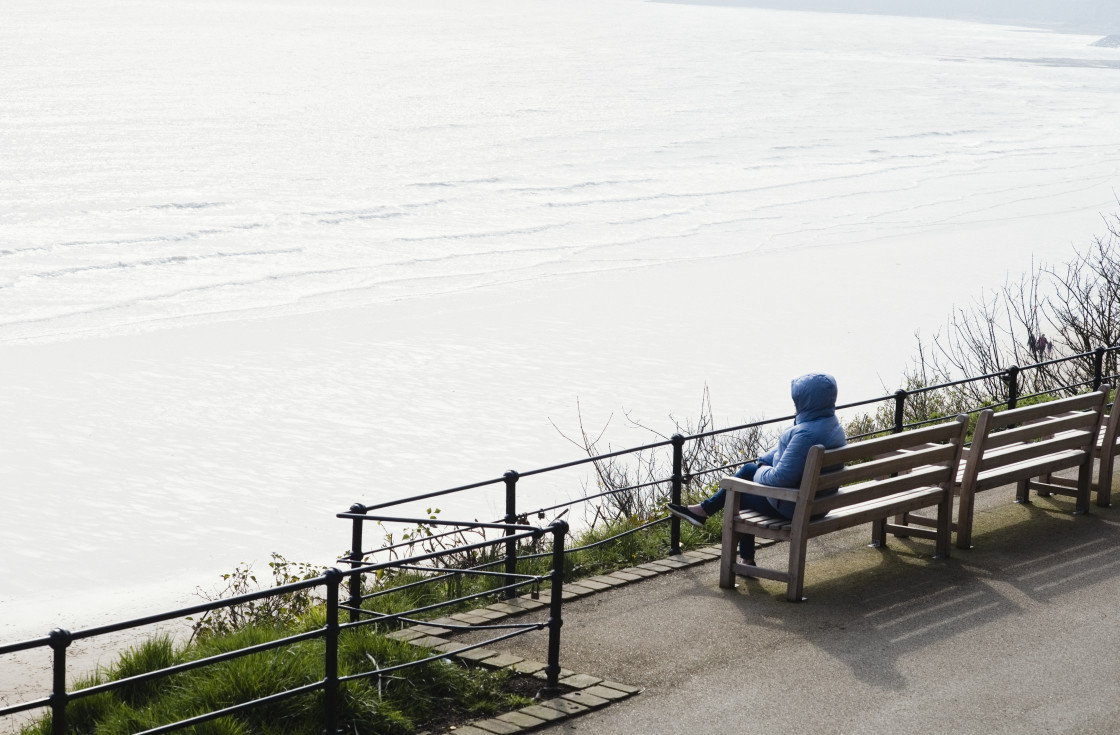 "A lone hooded woman enjoying winter sun overlooking Scarborough south bay" stock image