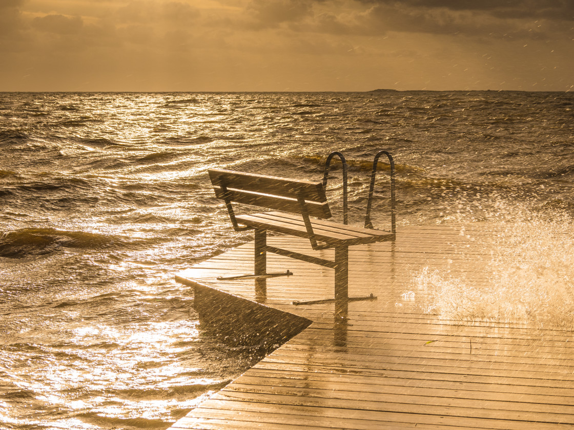 "Solitary Bench on a Wooden Pier Facing a Rough Sea During a Golden Sunset" stock image