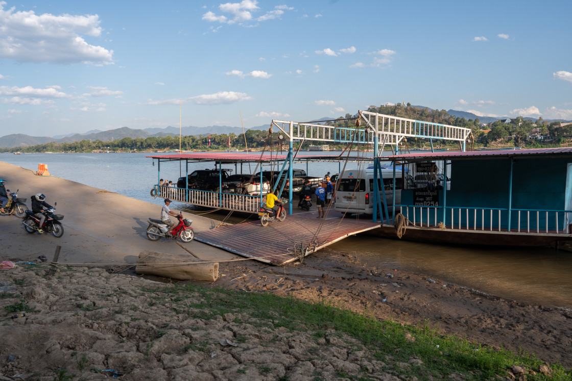 "A Laotian ferry boat carries motorcycles, scooters, assorted vehicles and passengers from one bank of the Mekong River to the other in Luang Prabang Laos Asia" stock image