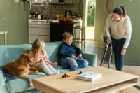 An adult vacuuming the living room with a Flexit central vacuum while two children and a dog sit on the sofa