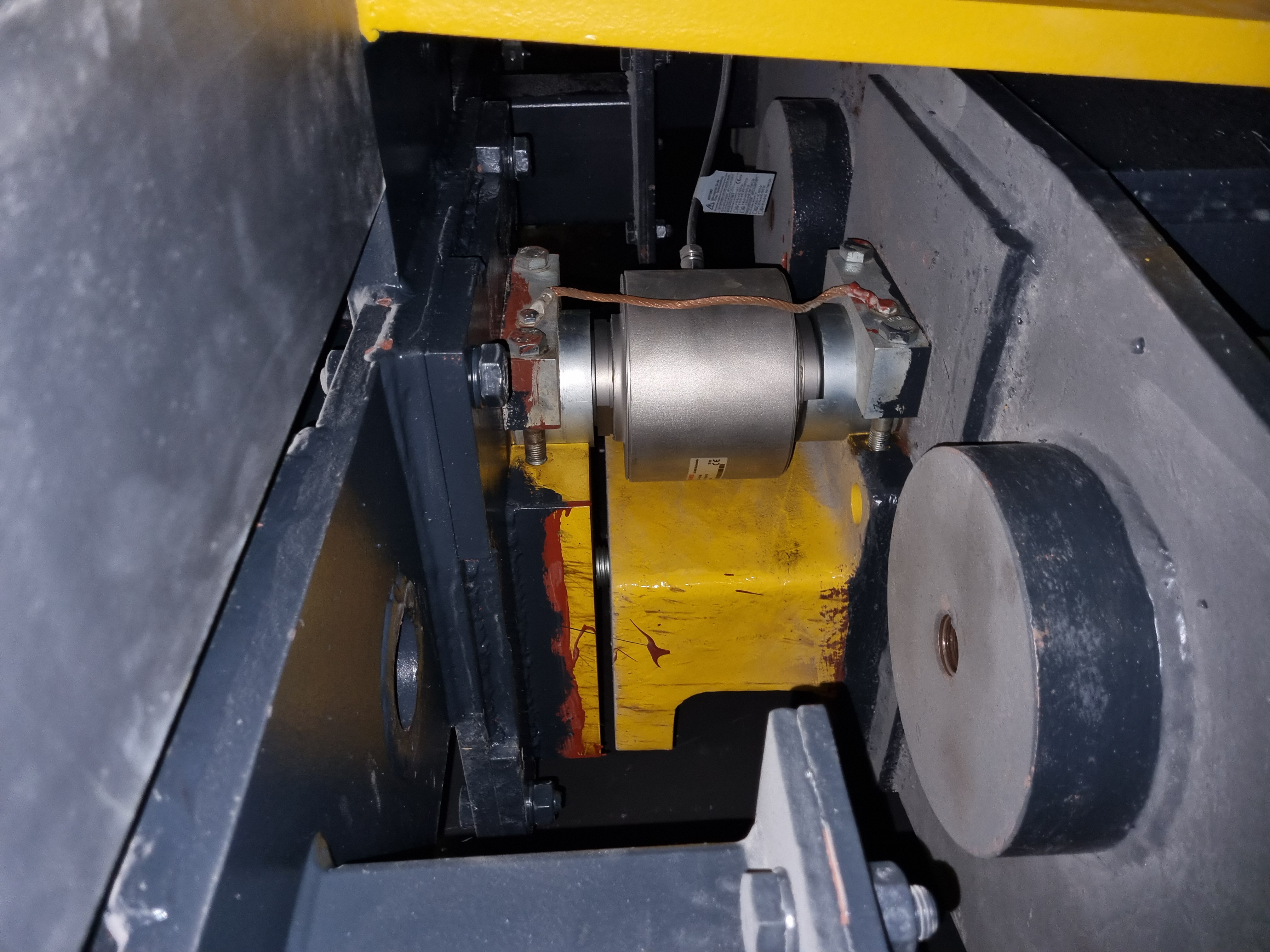 Cylindrical sensor installed between steel mounting plates in yellow and black stage machinery.