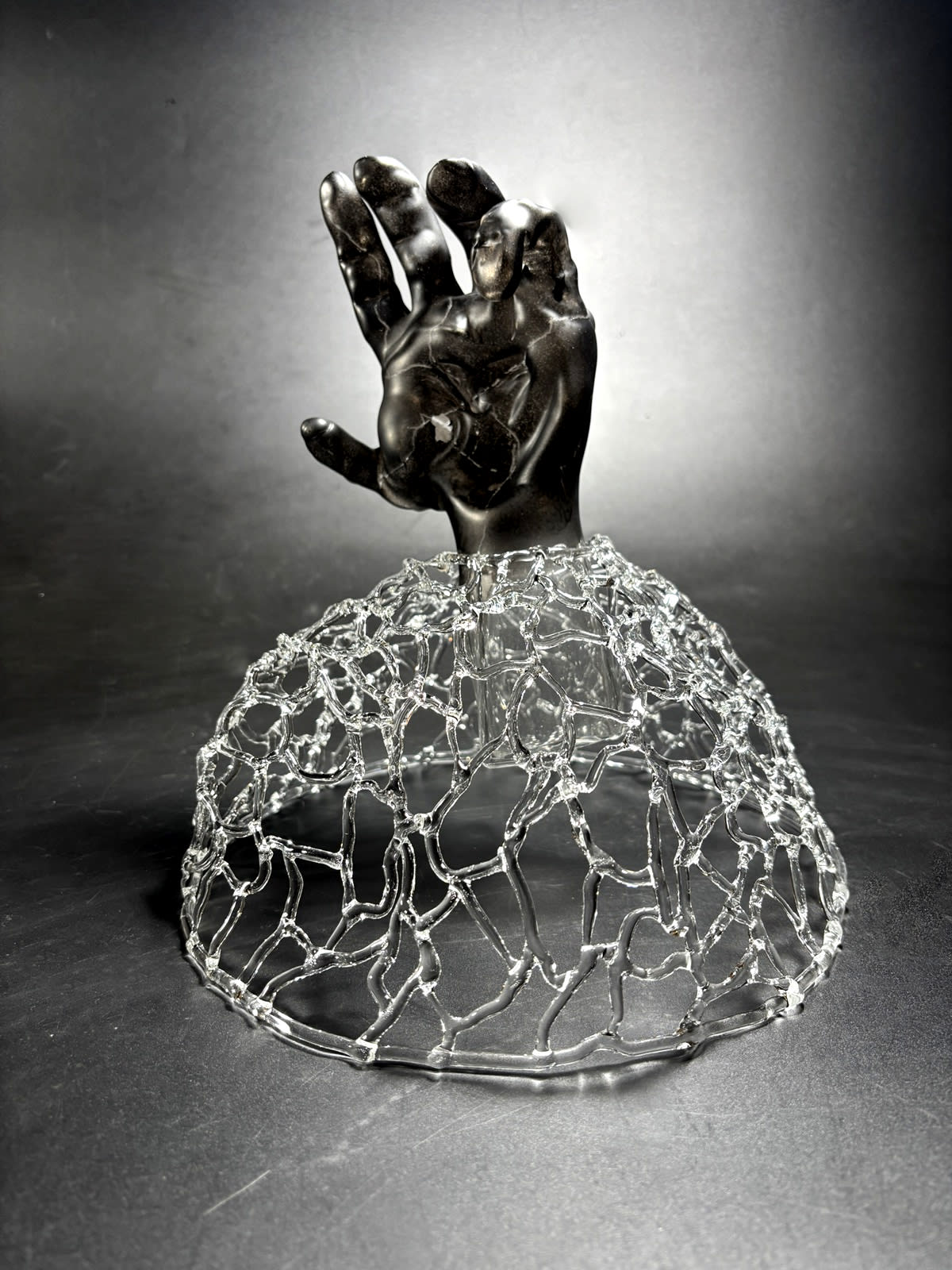 a life-sized soot-coated hand with cracks etched into it emerges from a networked base.