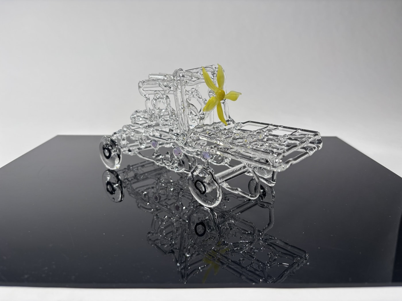 a model truck networked in glass with a yellow flower on the back of the cab, placed on a reflective panel
