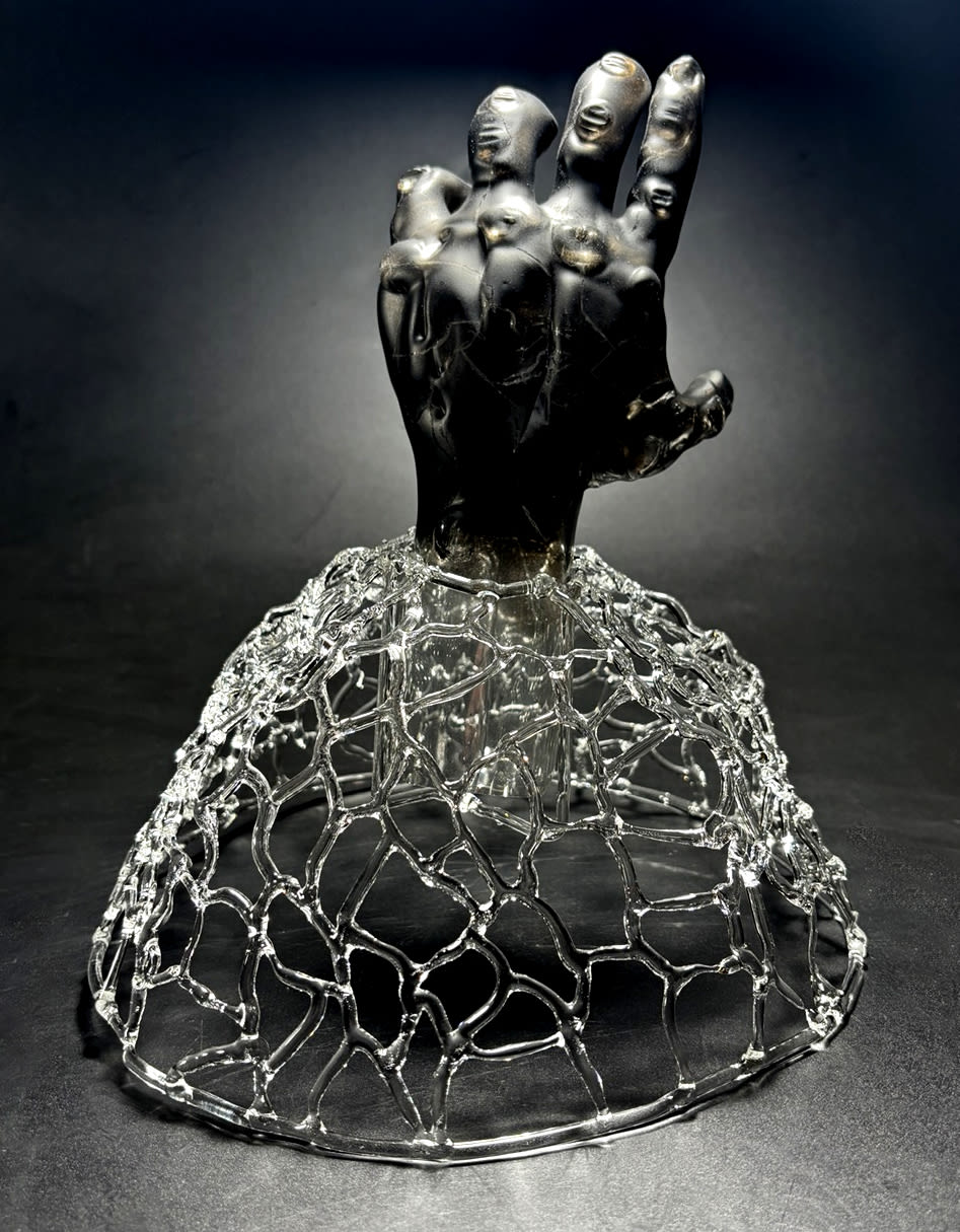 a life-sized soot-coated hand with cracks etched into it emerges from a networked base.