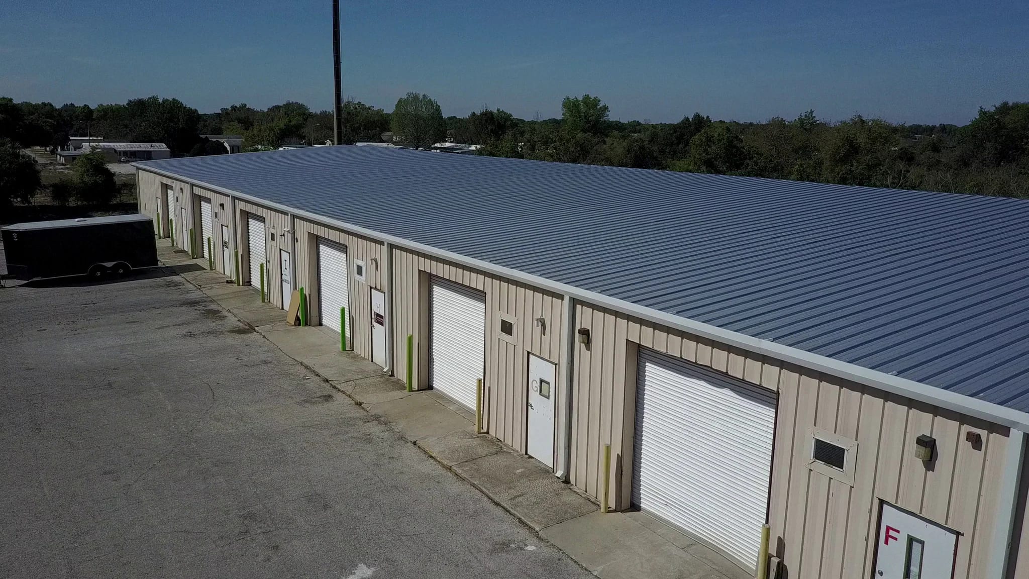 Row of white roll-up doors along a single-story small-bay industrial building under a blue sky.