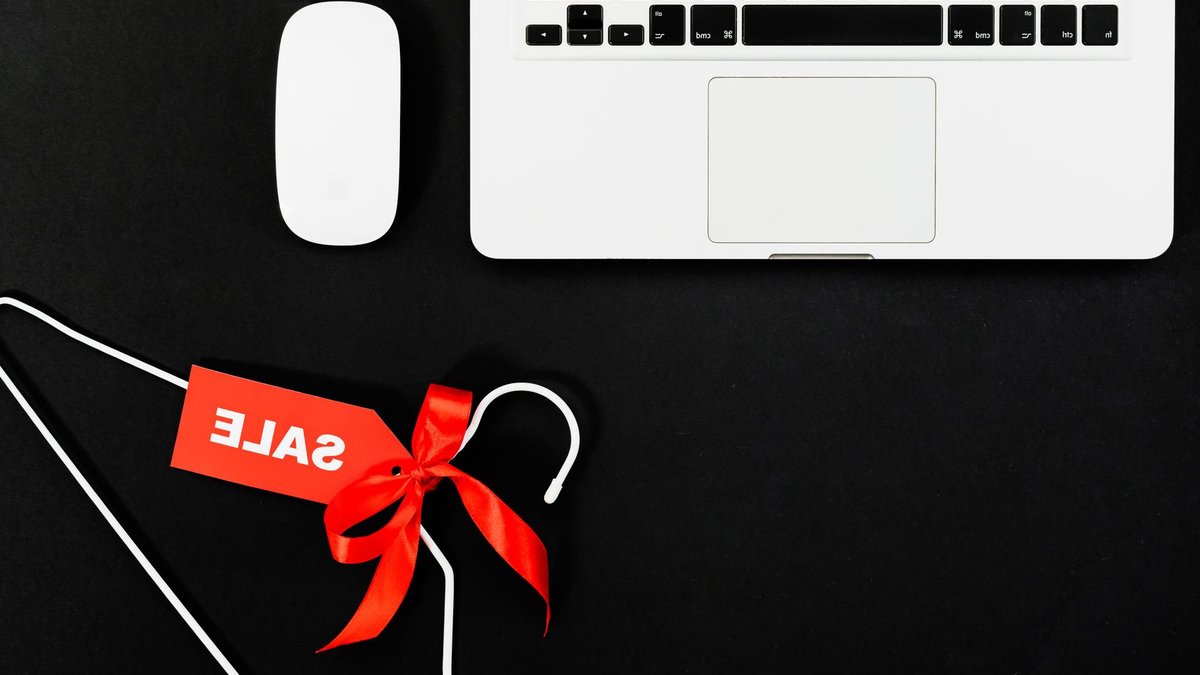 Stylish flat lay of a laptop, mouse, and sale tag on a hanger for online shopping concept.