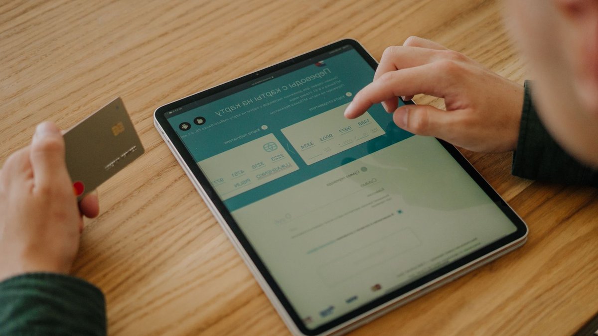 Fiserv launches platform overhaul under new CEO Person making an online payment using a tablet and credit card on a wooden desk.