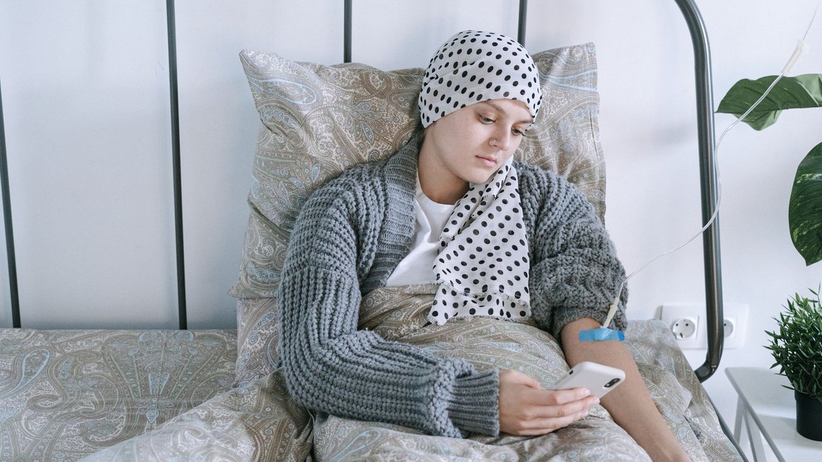 Woman undergoing cancer treatment at home, using a smartphone for support.