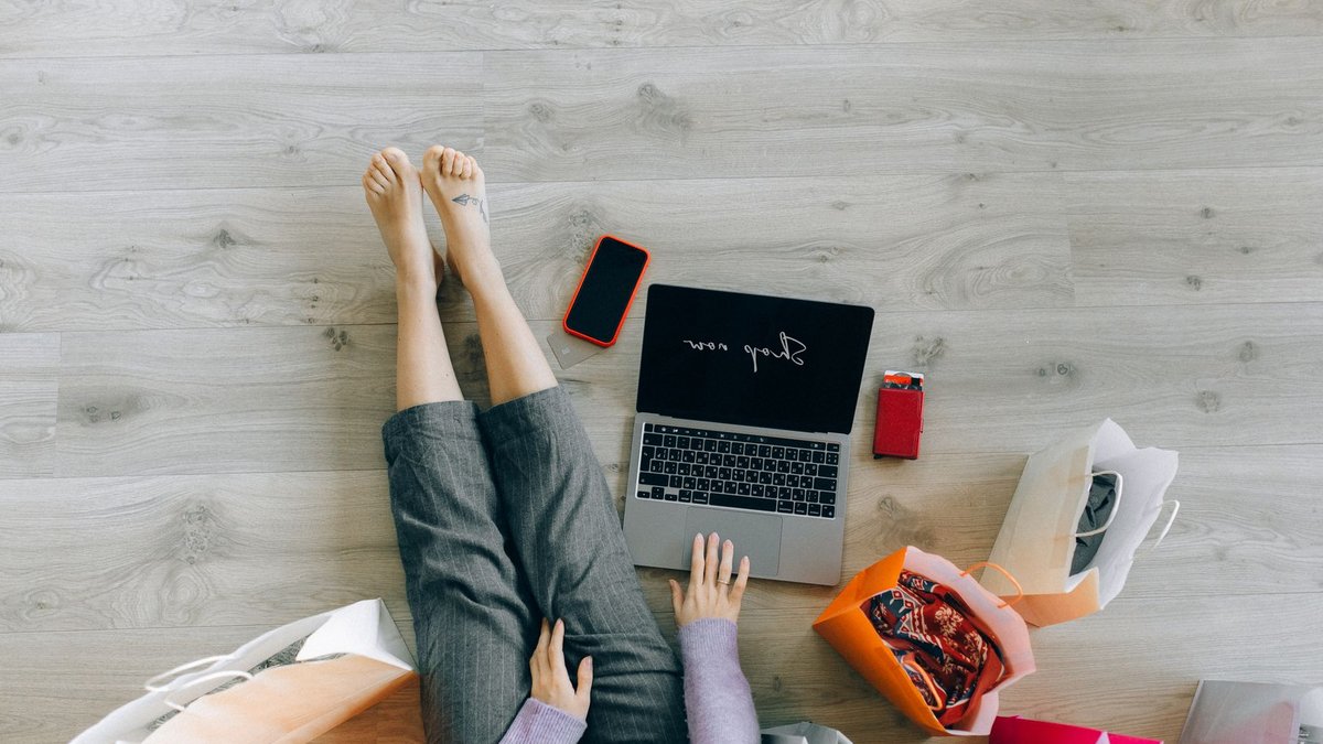 Woman shopping online with laptop and paper bags from above view.