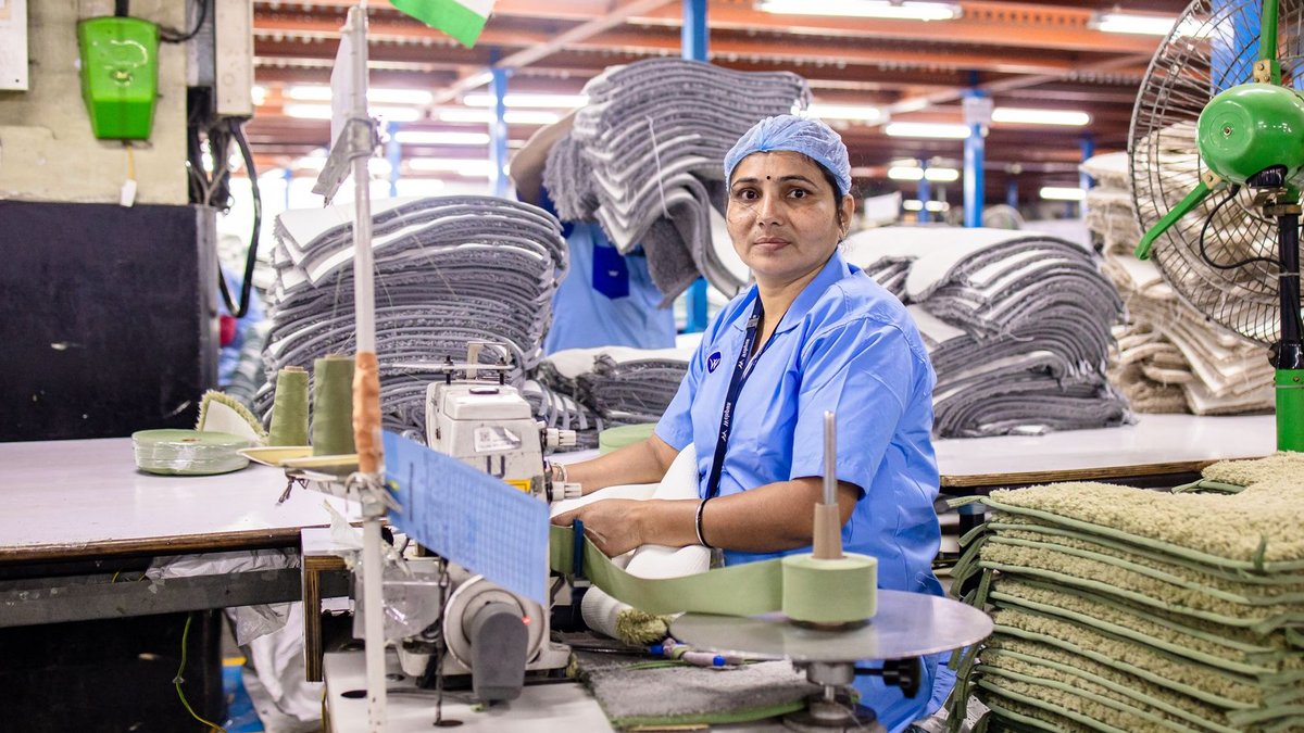 Indian conglomerate backs AI startup to enter global enterprise markets A female factory worker sewing textiles in an Indian factory, surrounded by fabrics.