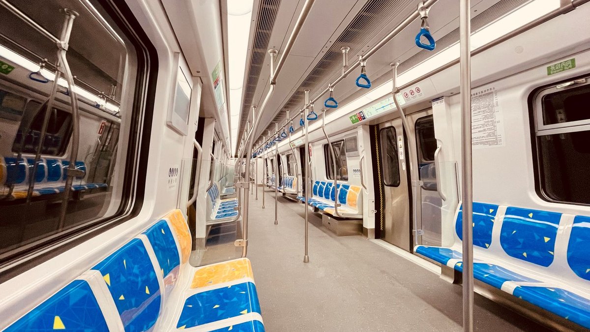 Wide-angle view of an empty train interior featuring bright blue and yellow seats and grab handles.