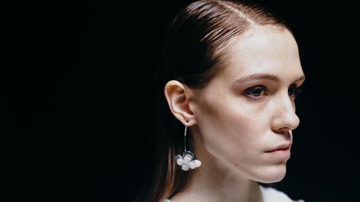 Portrait of a young woman with a floral earring against a dark background.