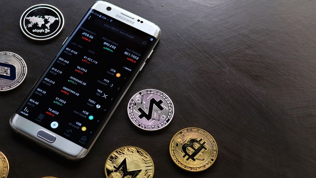 A collection of cryptocurrency coins and a smartphone displaying a digital trading platform.