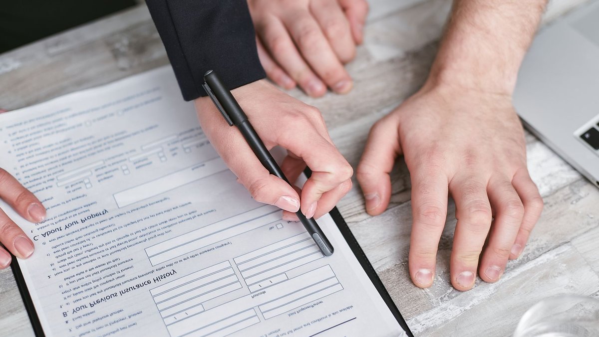Close-up image of two people signing an insurance policy document on a wooden desk.