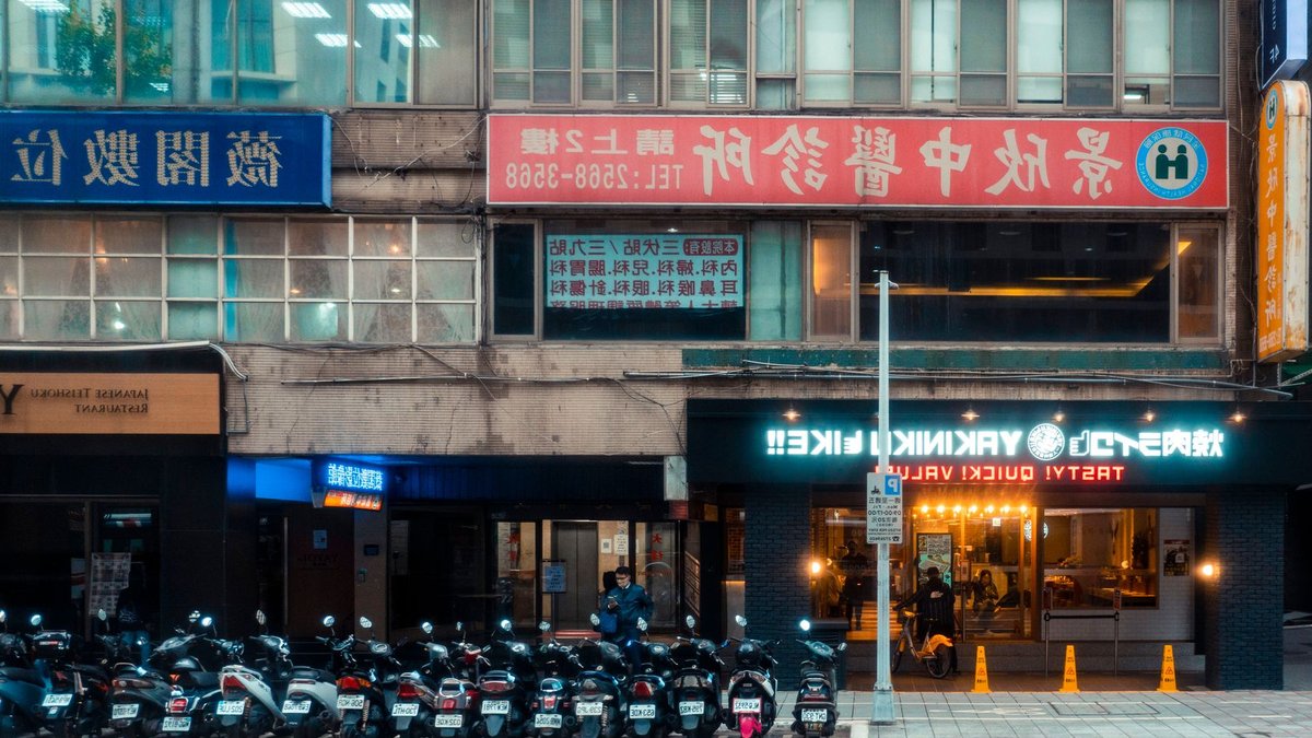 Daikoku NYC Revitalizes Chinatown Through Car Culture Busy urban street with restaurants, signage, and parked motorcycles, capturing city life dynamics.