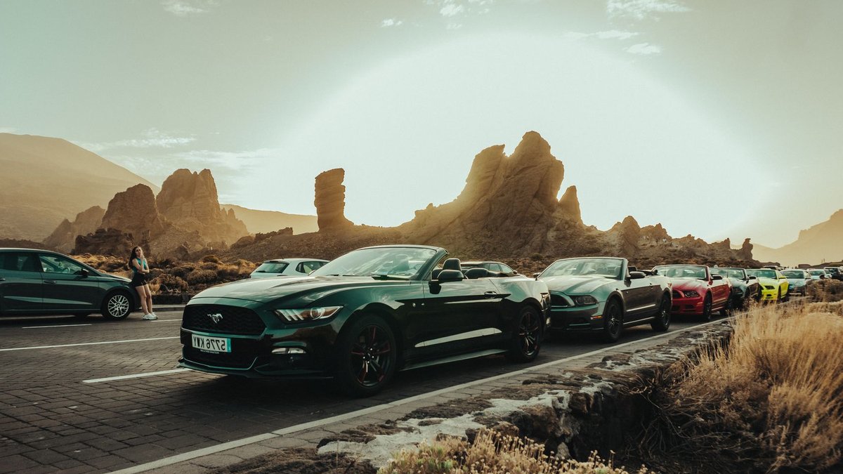 Cars lined up on a scenic road with striking rock formations during sunset.